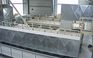 Langer, metallischer Prozessfilter mit umlaufendem Wartungssteg und Geländer, installiert in einer Industriehalle.