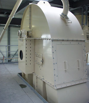 Großer, vertikaler Kettenelevator in heller Lackierung, mit abgerundetem Gehäuse und angeschlossenen Förderleitungen, installiert in einer Industrieanlage.